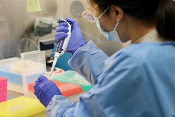 A lab technician wearing a blue gown and nitrile gloves works with a sample in the Public Health Laboratory